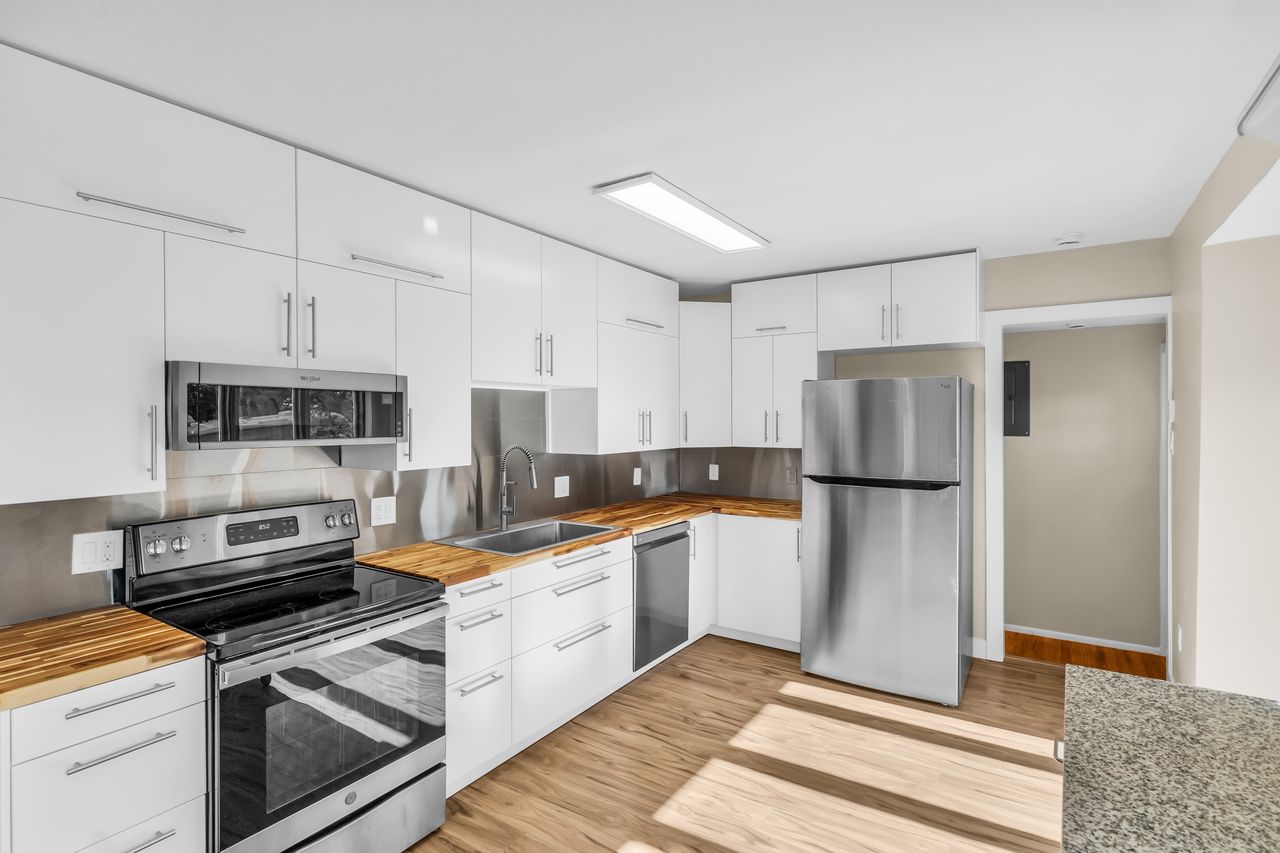 Kitchen featuring white cabinetry, wood-finish countertops, stainless steel appliances, and a metal backsplash
