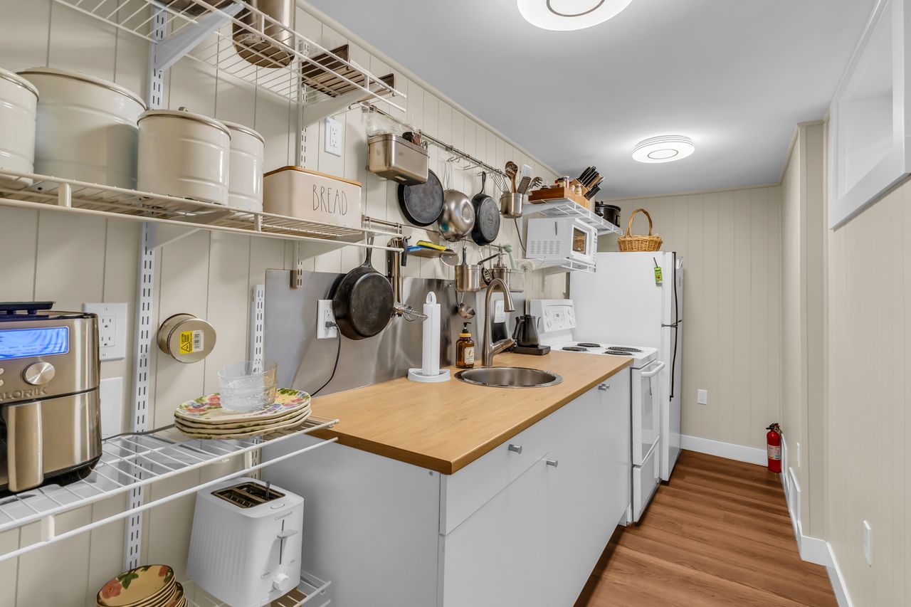 Compact kitchen featuring a stainless steel sink, wood-finish countertop, and white cabinetry. Plumbed for stackable laundry as well.
