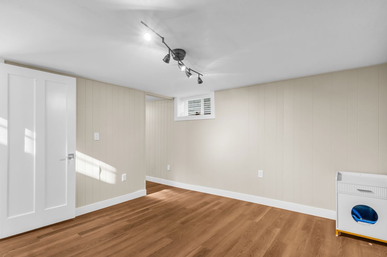 Spacious interior room featuring wood-finish flooring, white baseboards, and light-toned paneled walls