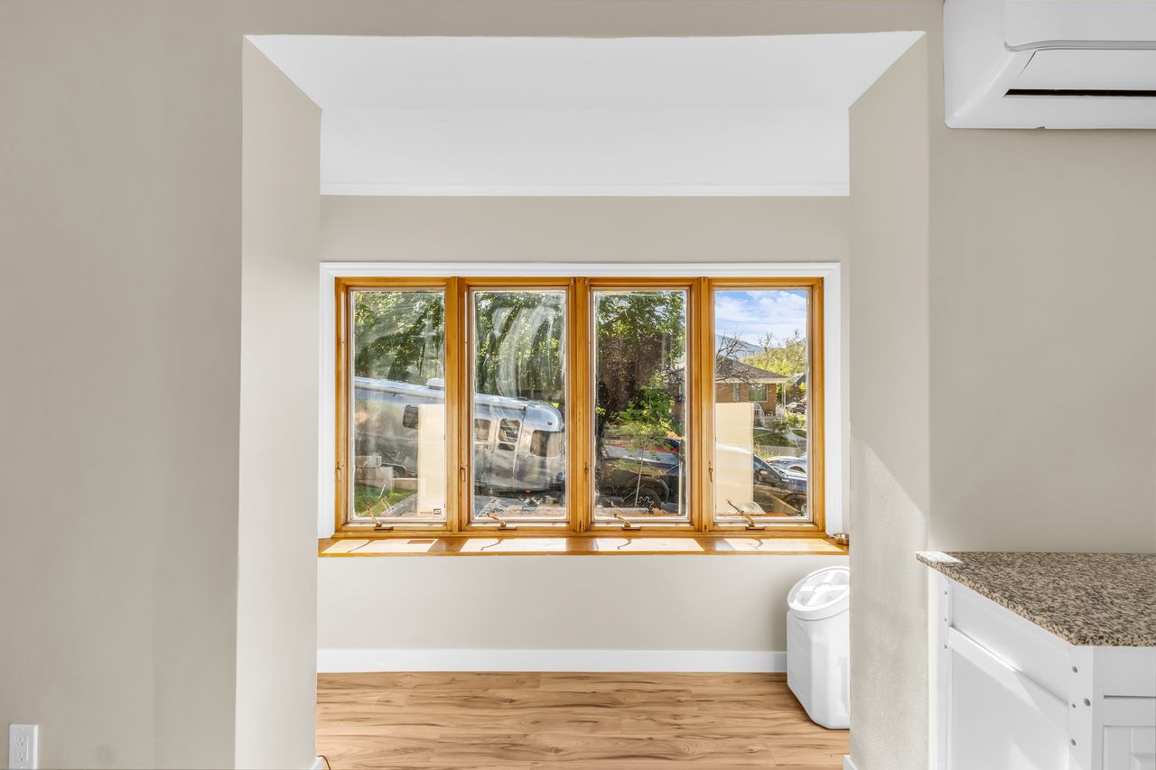 Bay window with natural wood trim, light wood-finish flooring, neutral wall paint, and a wall-mounted mini-split system