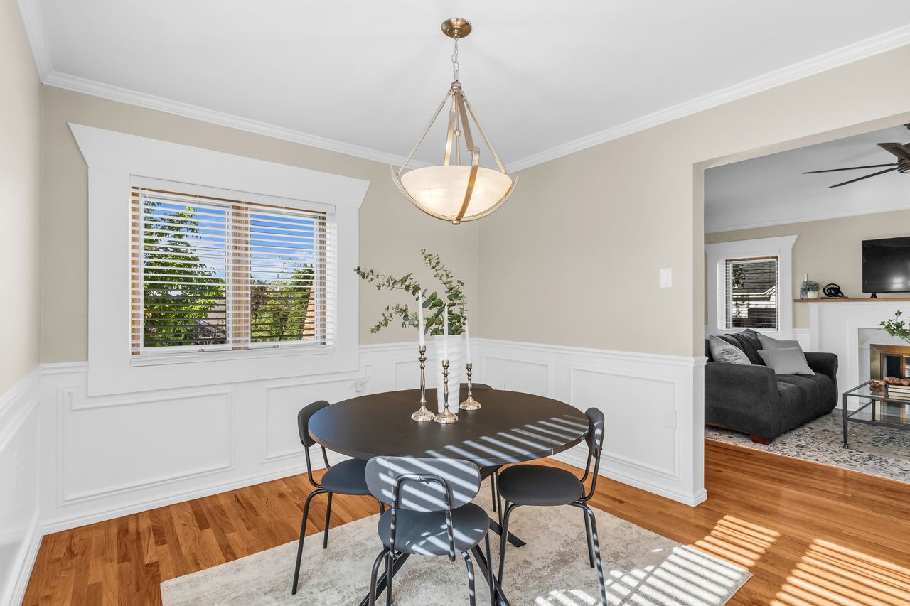 Dining area featuring wood-finish flooring, wainscoting, crown molding, a decorative chandelier, and a large window with blinds