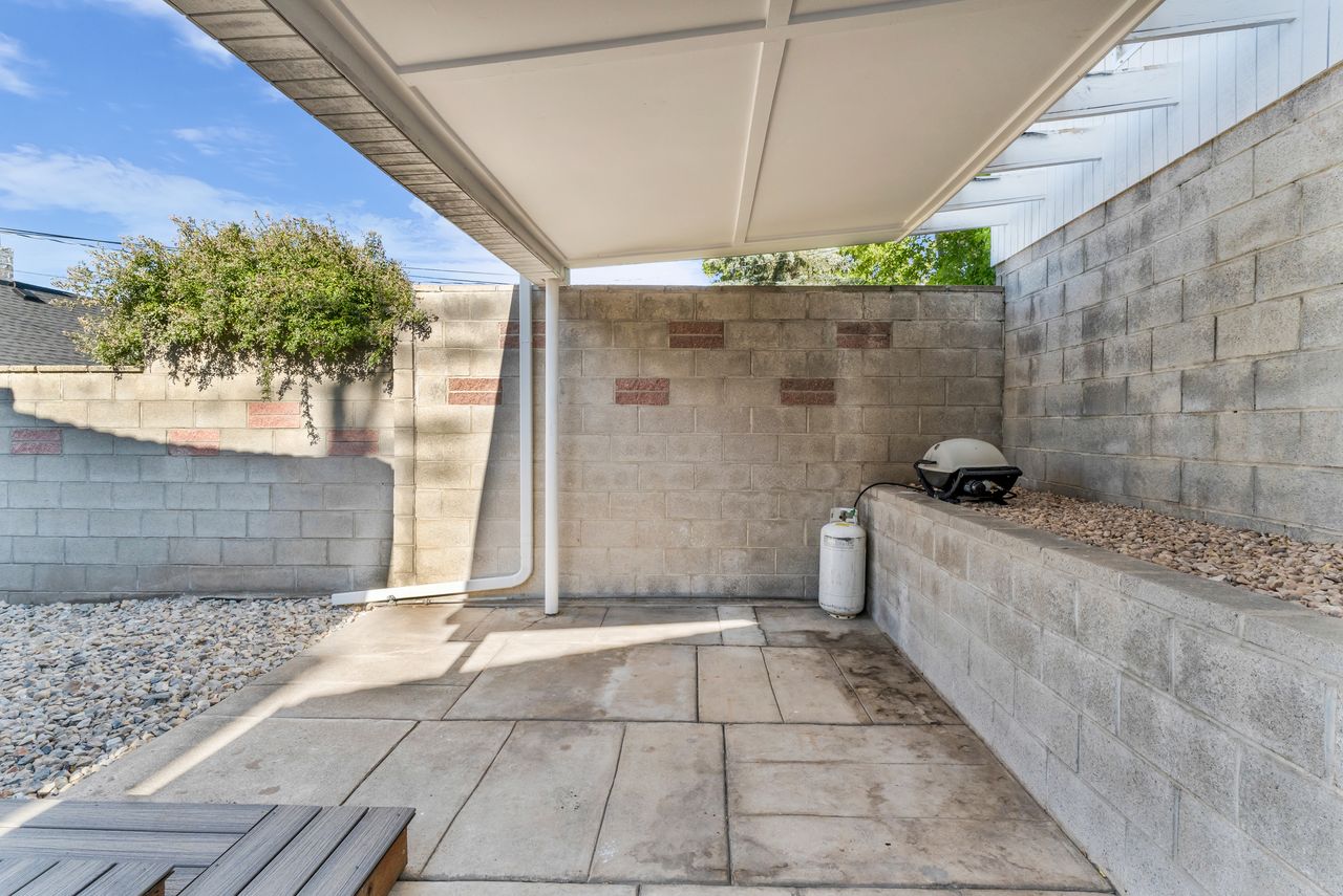 Outdoor patio area featuring concrete paver flooring, a white overhead pergola structure, and surrounding concrete block walls