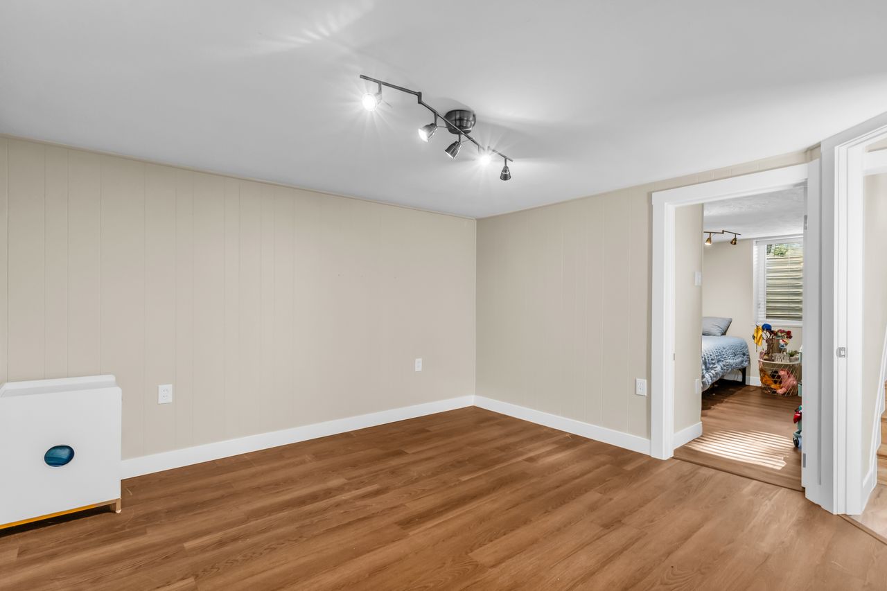 Expansive room featuring wood-finish flooring, light neutral paneling, track lighting, and white baseboards