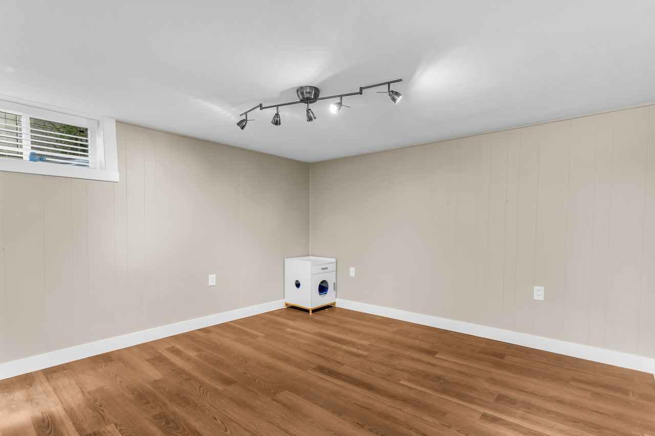 Spacious room featuring wood-finish flooring, light-colored vertical paneling, and a track lighting fixture