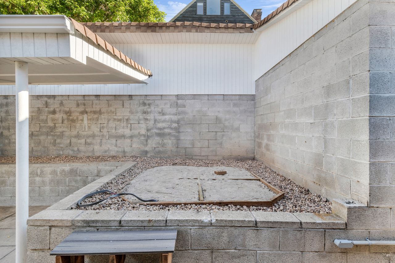 Enclosed outdoor area featuring multiple concrete block retaining walls, a gravel border, and wired for a hot tub