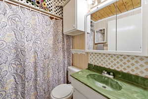 Bathroom featuring a green cultured marble vanity with an integrated sink, a mirrored medicine cabinet, and white upper cabinetry