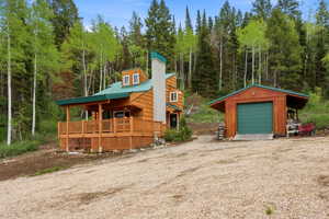 Wood-sided cabin featuring a covered porch with wood railings and lattice skirting, a green metal roof, and a prominent stone chimney