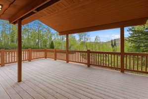 Expansive covered deck featuring wood-finish flooring, a wood-finish railing, and exposed wood ceiling beams