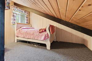 Attic space featuring light wood-paneled walls and sloped ceilings with exposed dark wood beams