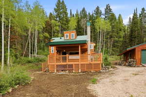 Log cabin featuring a green metal roof, a full-width front porch with a wood railing, and a stone chimney