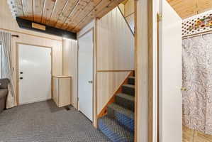 Interior hallway featuring wood paneling, wood plank ceiling, carpeted stairs, and multiple doorways