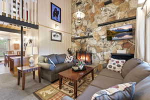 Living area featuring a floor-to-ceiling natural stone fireplace with a metal fire screen, wood-finish flooring, and a second-story balcony with white railings