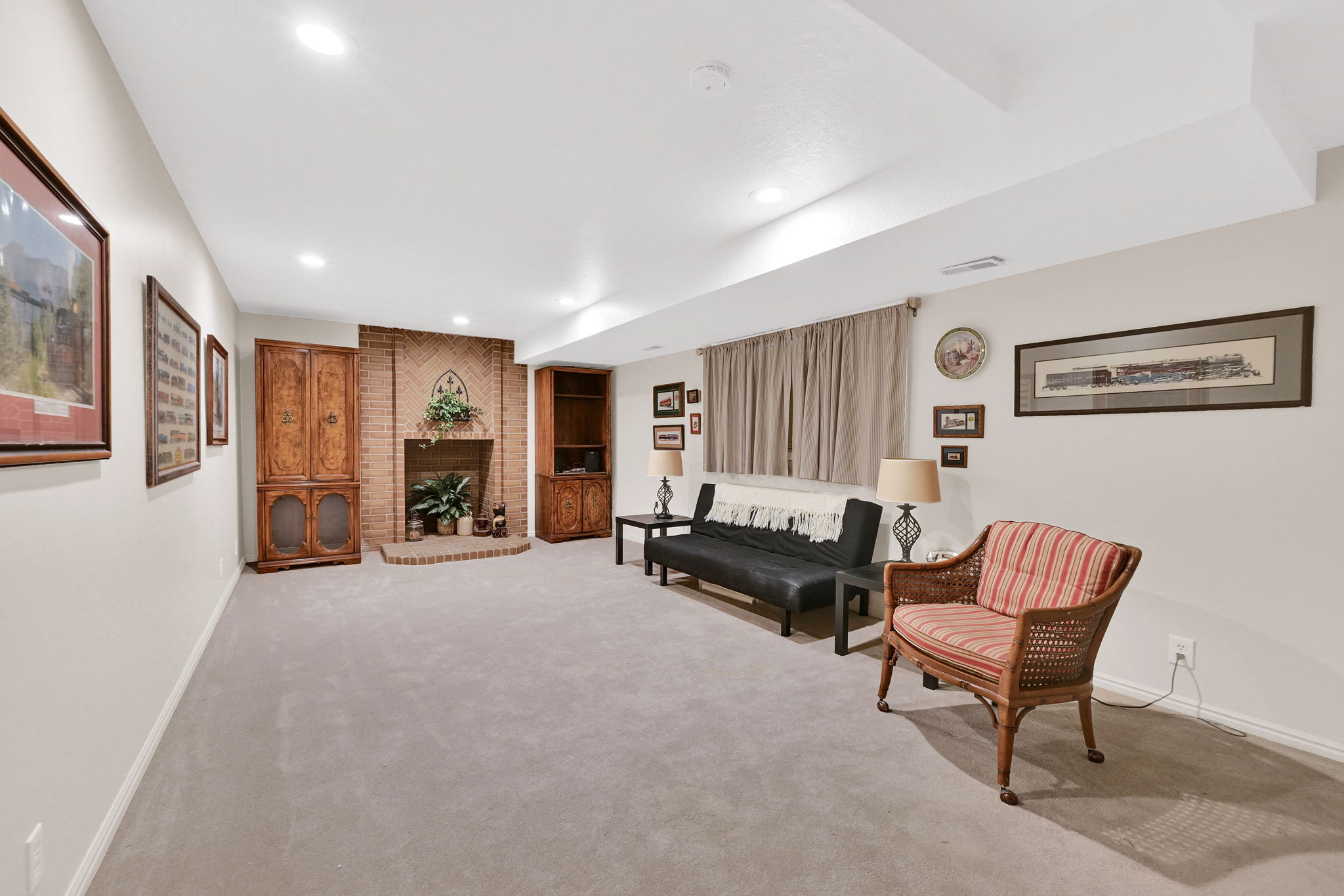 Spacious interior room featuring a brick fireplace area with a raised hearth, recessed lighting, and light-toned wall-to-wall carpeting