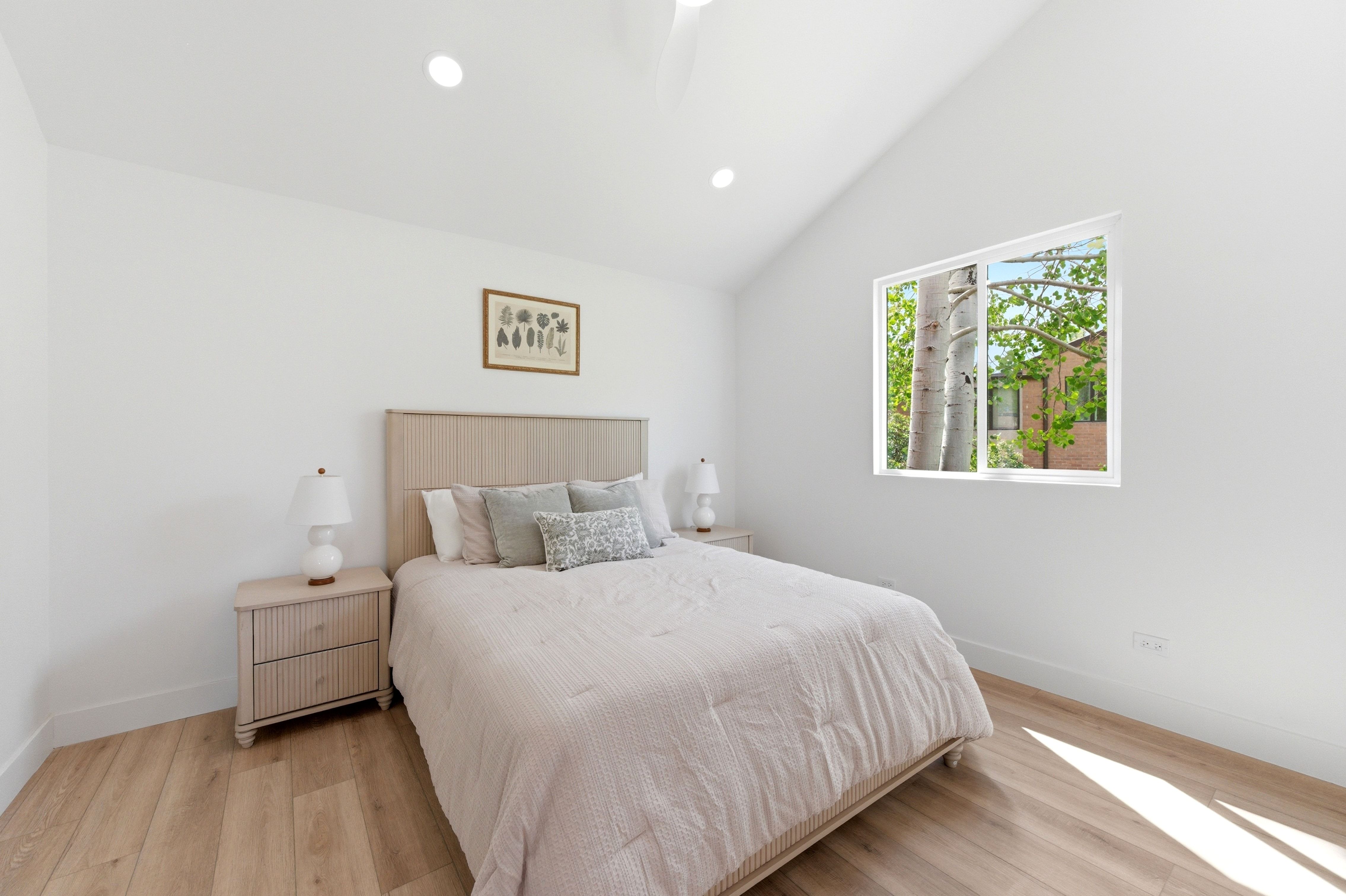 Vaulted ceilings with recessed lighting, wood-finish flooring, and a large window