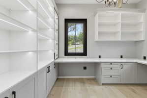 Built-in custom cabinetry with integrated lighting, a spacious L-shaped desk with a light-toned countertop, and wood-finish flooring