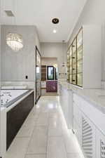 Elongated bath area featuring a built-in jetted tub with dark-toned paneling, a large mirror, and a contemporary chandelier