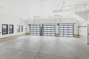Spacious multi-car garage featuring three contemporary glass-paneled doors, concrete flooring, multiple windows with black frames, and exposed ceiling ductwork