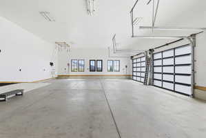 Spacious garage with concrete flooring, two contemporary overhead doors, multiple windows with dark framing, bright overhead lighting, and built-in utility connections