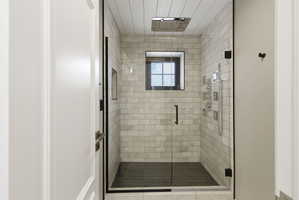Glass-enclosed shower with subway tile walls and dark herringbone-patterned floor