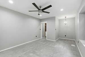 Spacious room featuring light gray carpeting and walls, a modern ceiling fan, recessed lighting, and a crystal chandelier