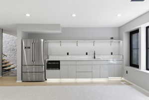 Modern wet bar featuring a stainless steel French-door refrigerator, integrated microwave, undermount sink with a matte black faucet, and light gray cabinetry with under-cabinet lighting