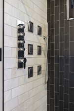 Shower featuring an integrated control panel with multiple body sprays, a handheld shower fixture, and contrasting subway tile in black and white finishes