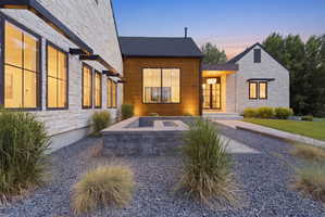 Modern exterior featuring a stone facade, wood-clad accents, a built-in fire pit, black-framed windows, and a gravel landscape