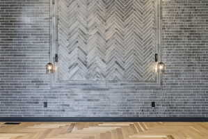 Herringbone wood-finish flooring complements a feature wall with gray subway tile and a central herringbone tile pattern