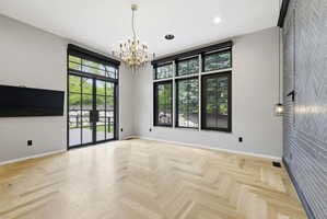 Spacious room with light wood-finish herringbone flooring, black-framed French doors, and transom windows