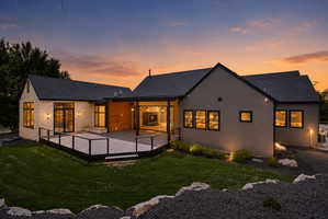 Expansive exterior featuring a large composite deck with cable railings, dual sliding glass doors, and recessed outdoor lighting