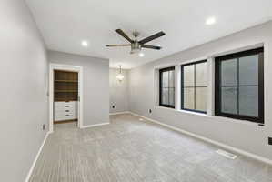 Room featuring three black-framed windows, a ceiling fan with light fixture, recessed lighting, and patterned carpeting