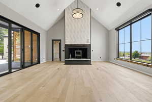 Vaulted living space featuring a modern fireplace with textured tile surround, expansive multi-panel windows, wide plank wood-finish flooring, and multi-slide patio doors