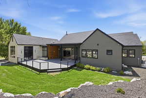 Expansive exterior featuring a large composite deck with cable railings, a covered patio area with a built-in fireplace, and a manicured lawn