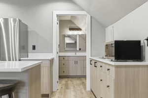 Compact kitchen area featuring stainless steel refrigerator, light-toned cabinetry with dark hardware, a sink, and white countertops