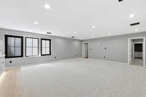 Spacious room featuring light gray carpeting, recessed lighting, and three black-framed windows