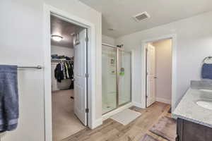 Bathroom featuring a glass-enclosed shower, dual vanity with light-colored countertop, wood-finish flooring, and a recessed ceiling light
