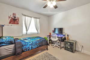 Carpeted room featuring a ceiling fan with light fixture, a window with blinds and drapery, and white walls