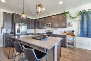 Kitchen featuring wood-finish flooring, dark wood cabinetry, stainless steel appliances, and a central island with a light-toned countertop