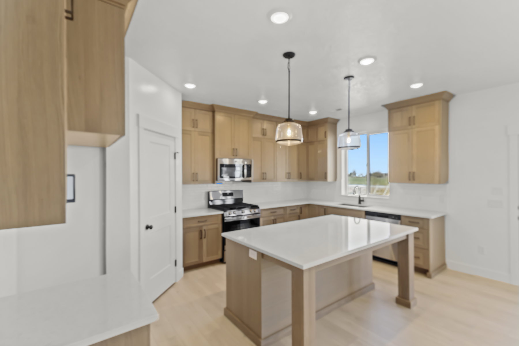 Spacious kitchen featuring light wood-finish cabinetry, a large center island with a white countertop, recessed lighting, and two pendant lights