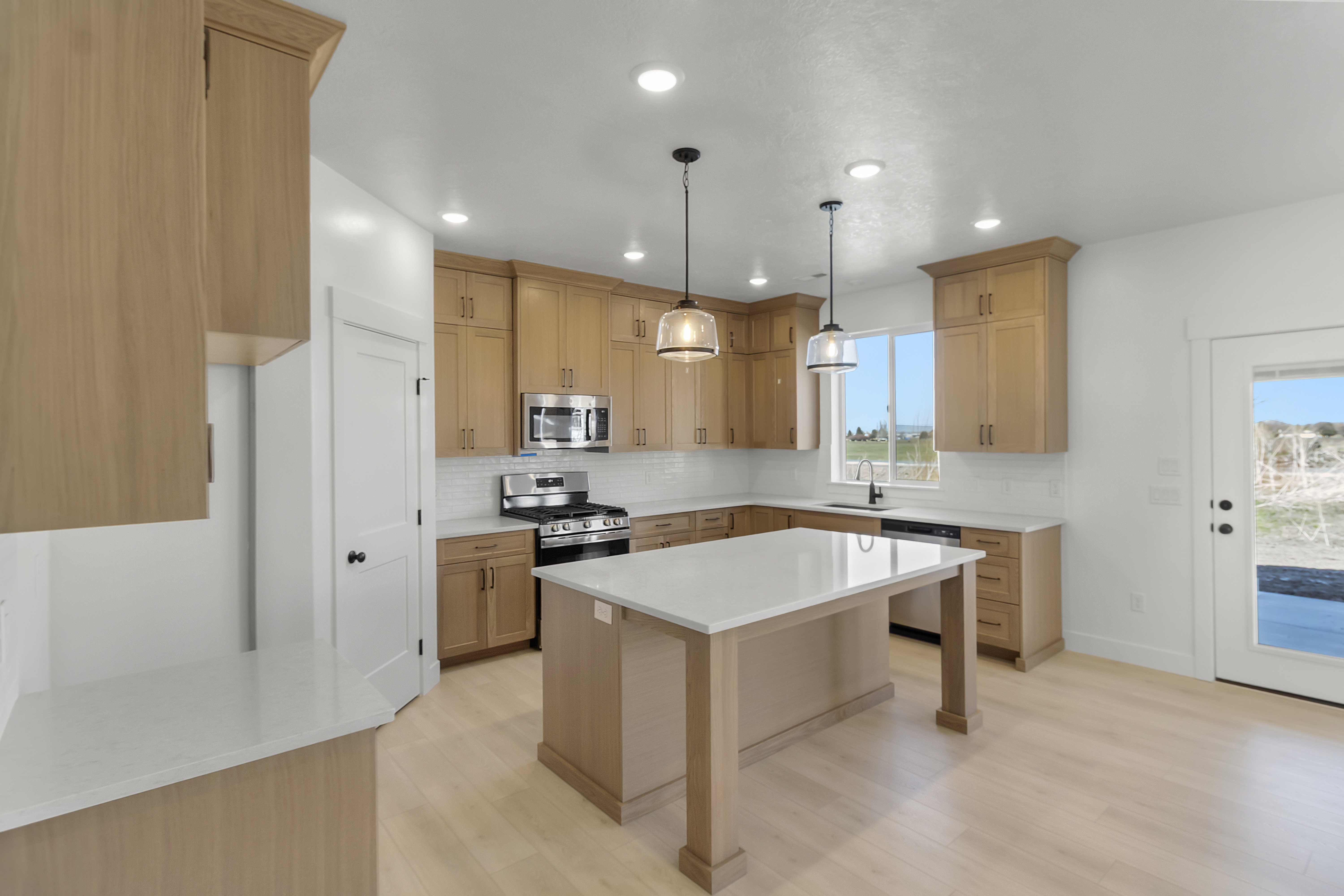 Modern kitchen featuring light wood-finish cabinetry, a central island with a solid surface countertop, stainless steel appliances, and wood-finish flooring