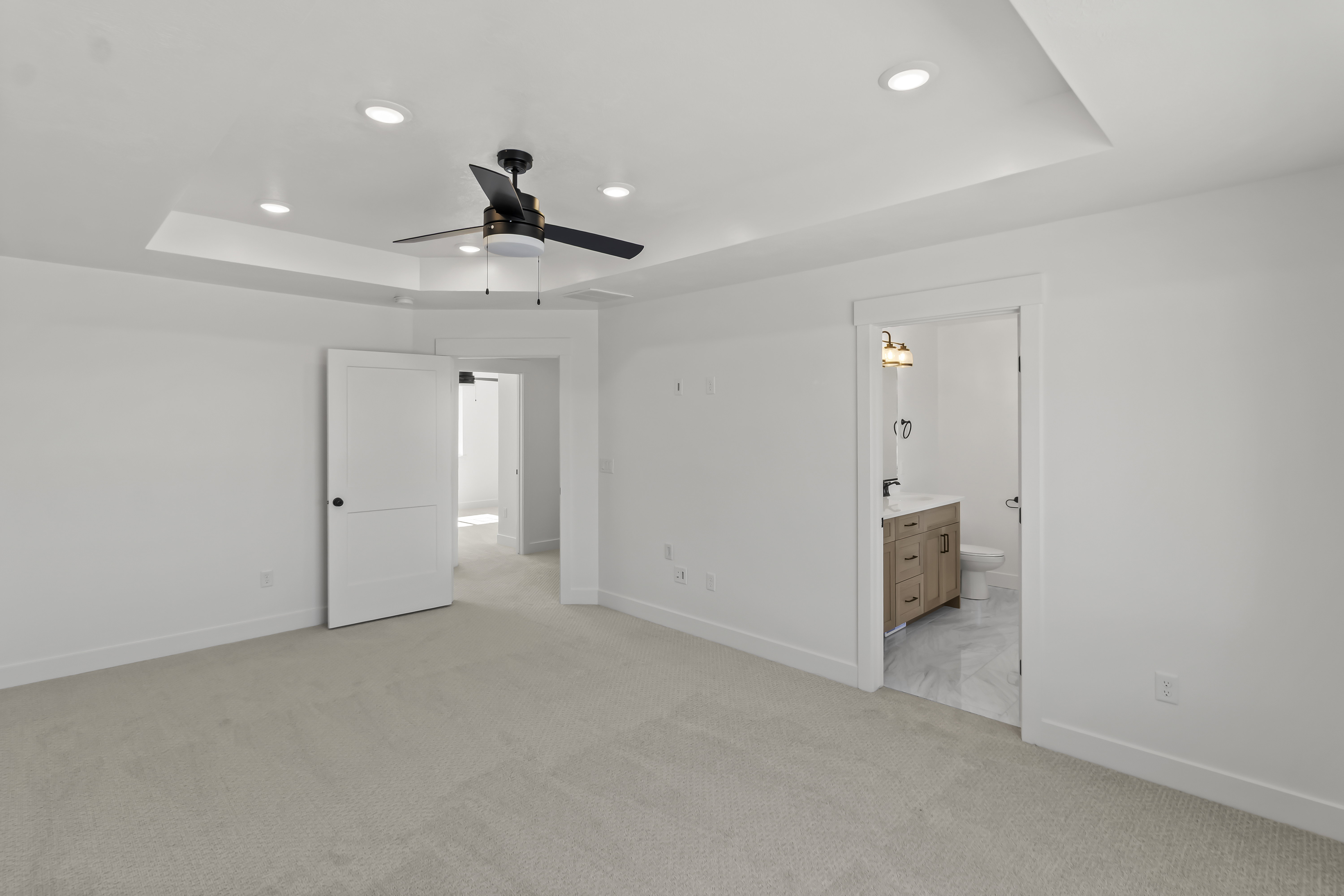 Spacious interior room featuring light-toned carpeting, a tray ceiling with recessed lighting, and a contemporary ceiling fan
