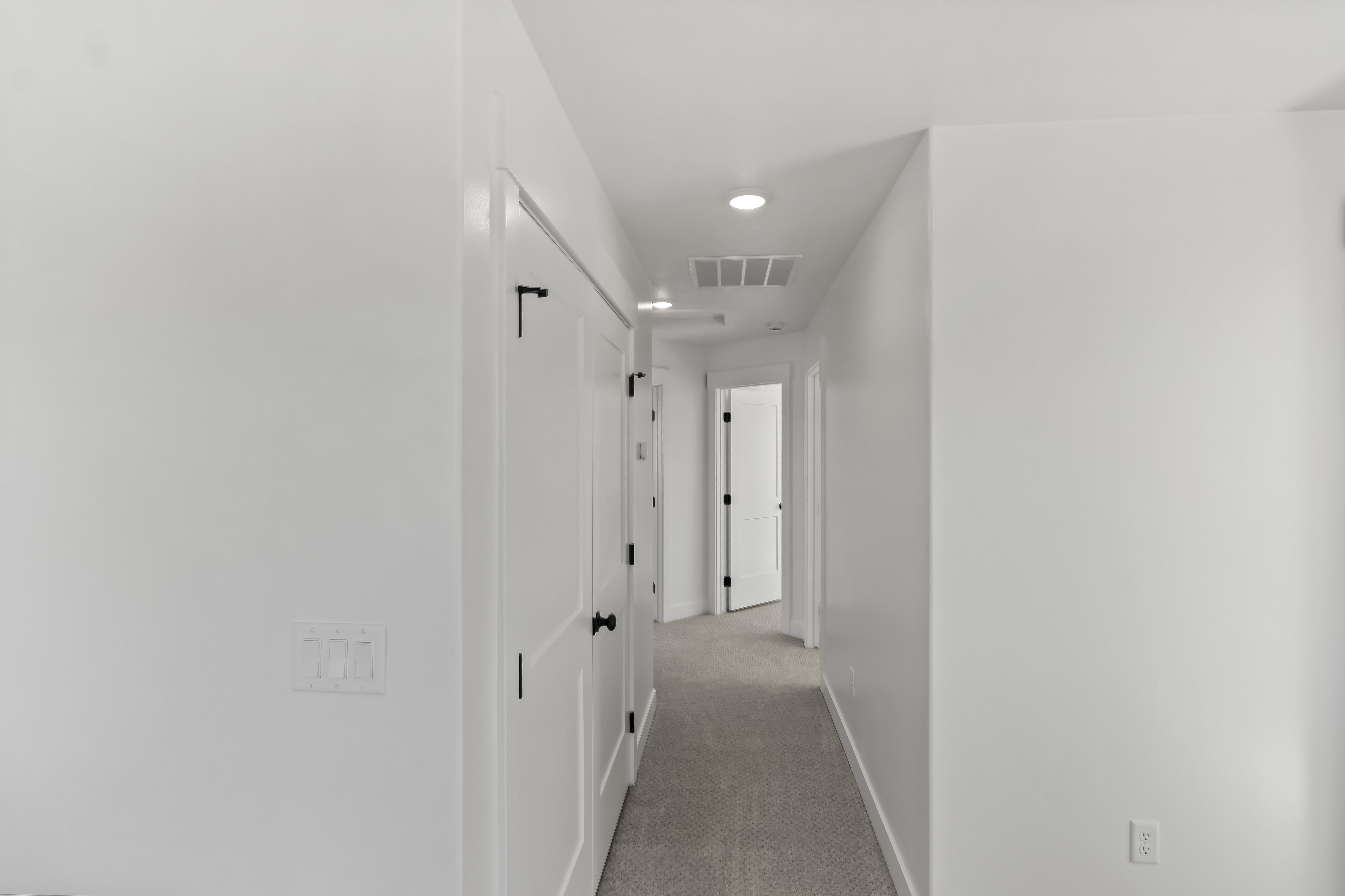 Hallway featuring recessed lighting, white paneled doors with matte black hardware, white walls, and light-toned carpet flooring