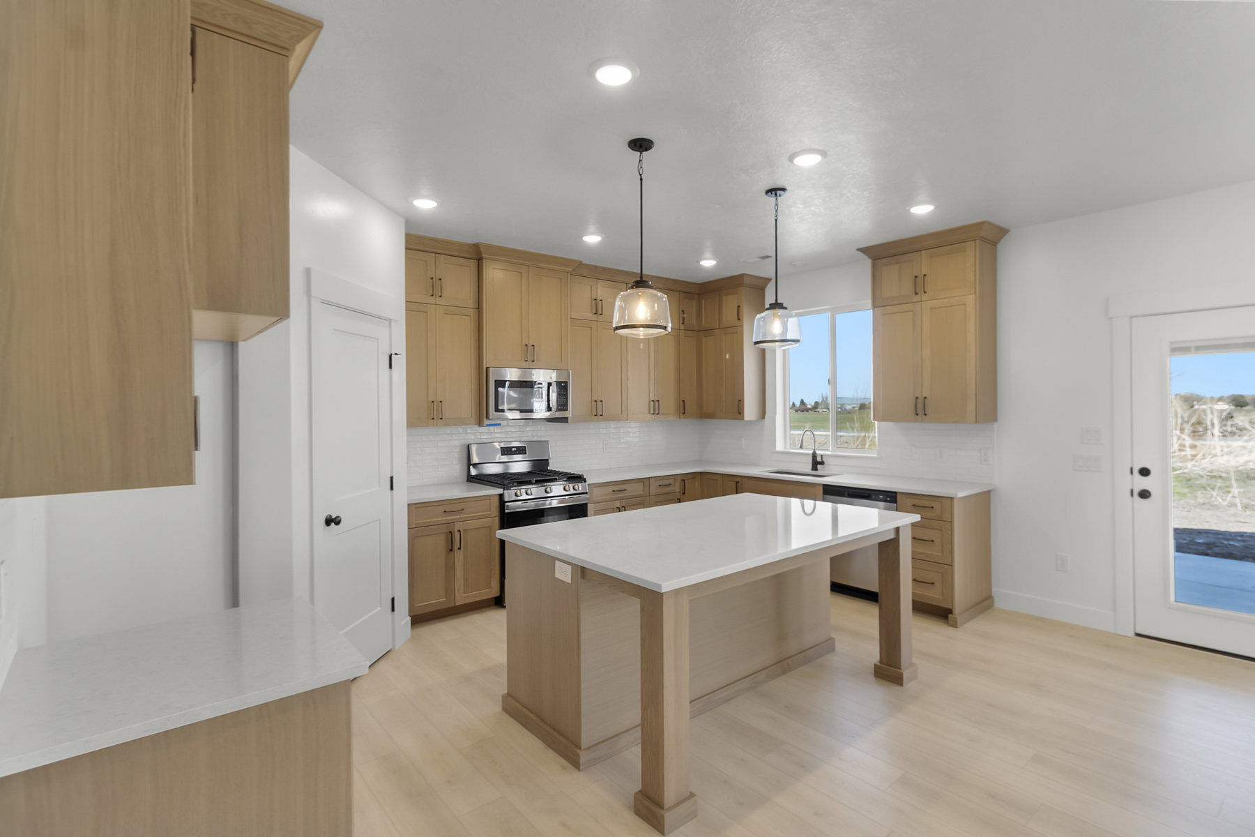 Kitchen featuring light wood-finish cabinetry, white subway tile backsplash, stainless steel appliances, and a central island with a white countertop