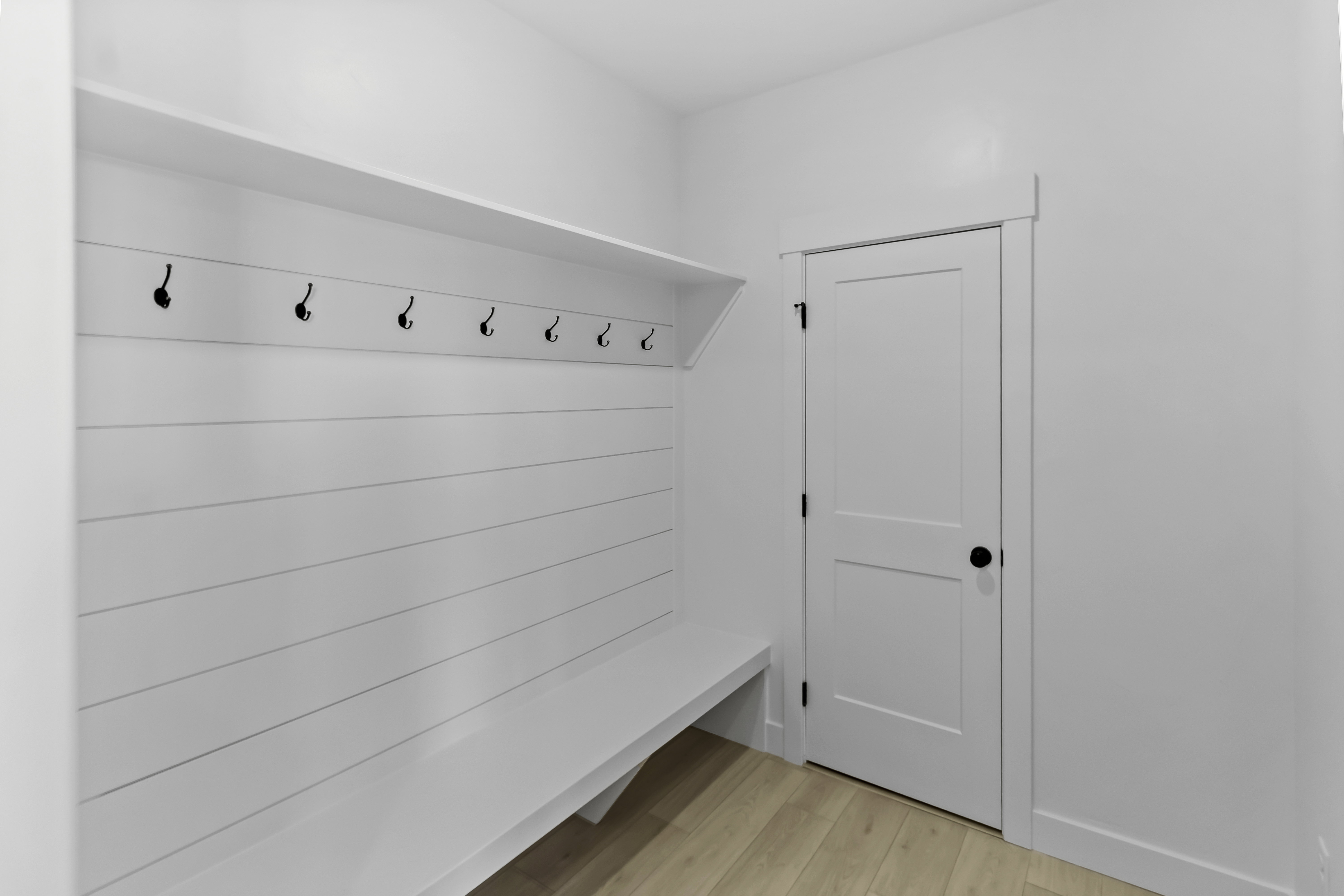 Built-in mudroom bench with shiplap backing, storage shelf, and multiple black coat hooks