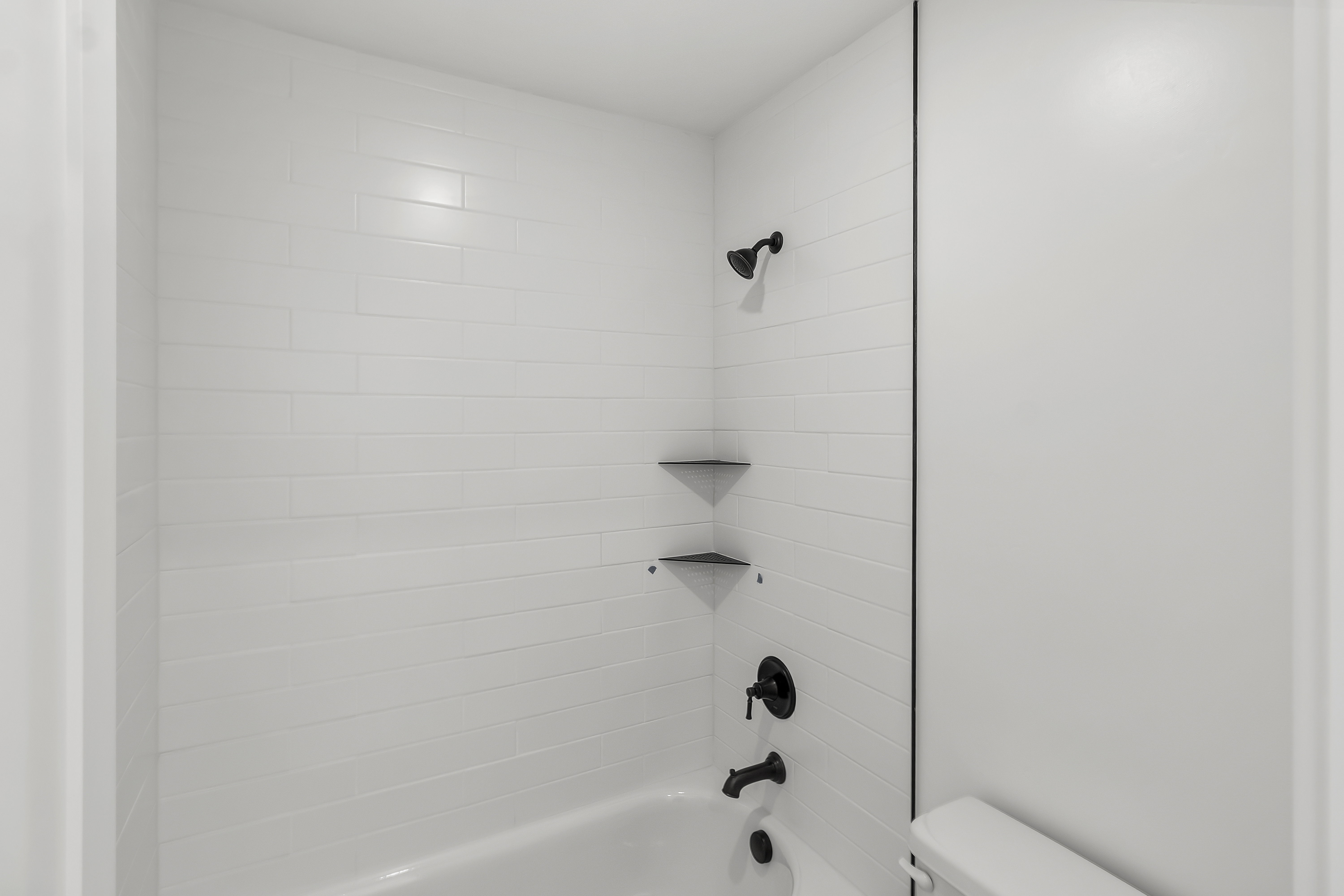 Bathtub with white subway tile surround, matte black shower fixtures, and integrated corner shelves