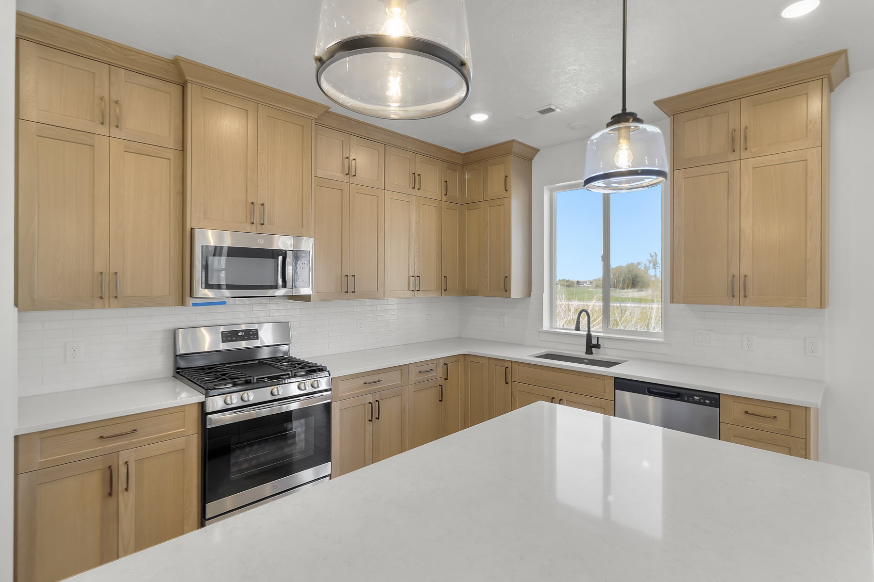 Modern kitchen featuring light wood-finish cabinetry, stainless steel appliances, white subway tile backsplash, and light countertops