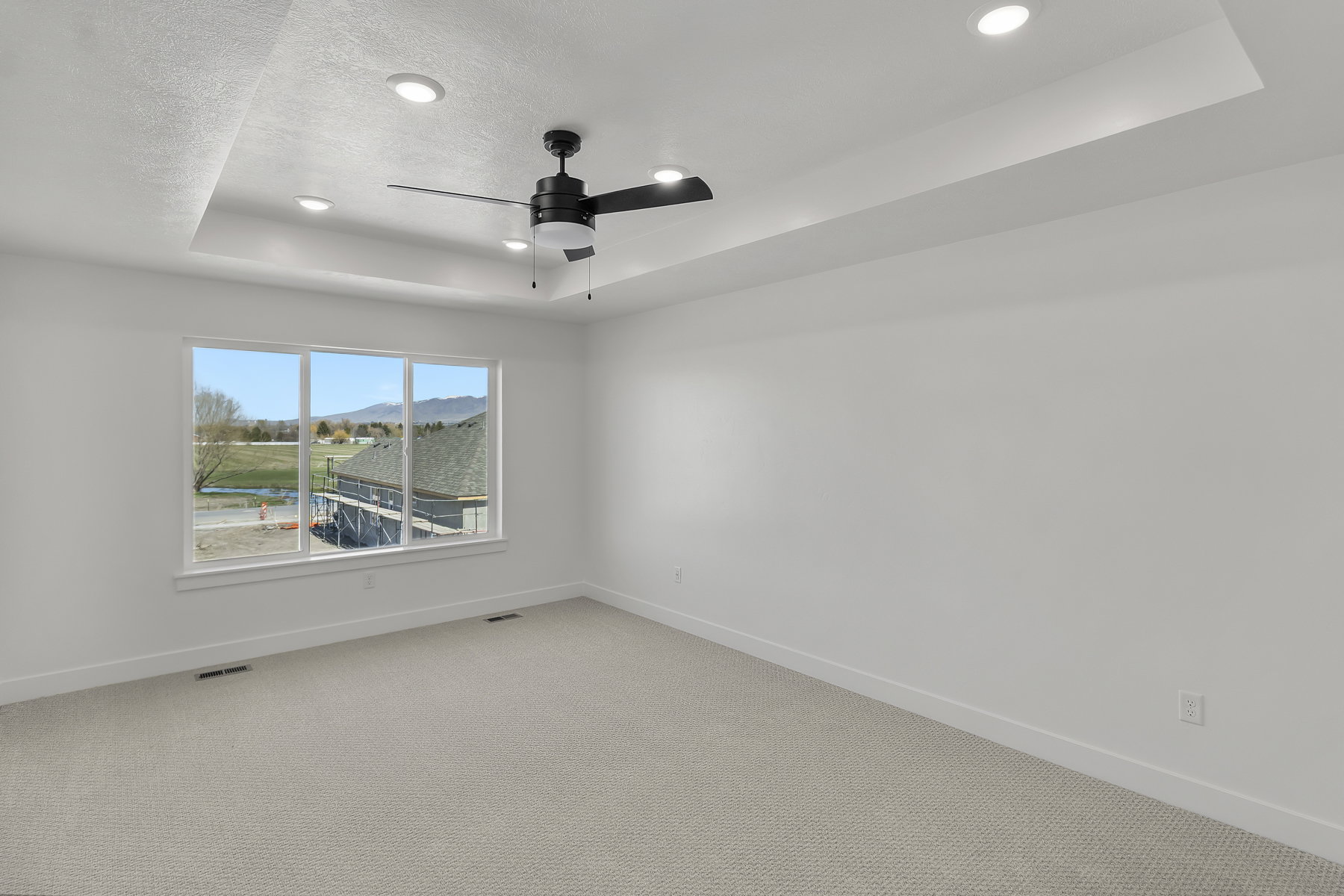 Spacious room featuring a tray ceiling with recessed lighting, a modern ceiling fan, large windows, and neutral carpeting