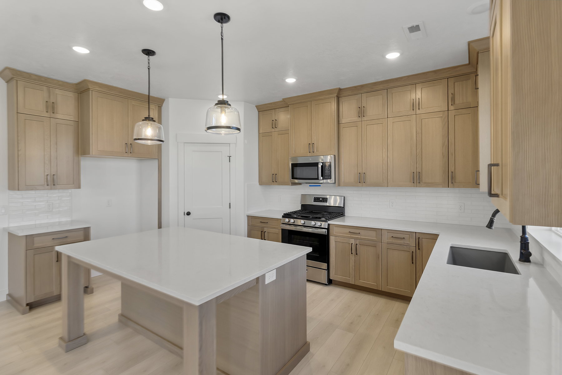 Kitchen featuring a central island with a solid surface countertop, light wood-finish cabinetry, stainless steel appliances, a subway tile backsplash, and recessed lighting