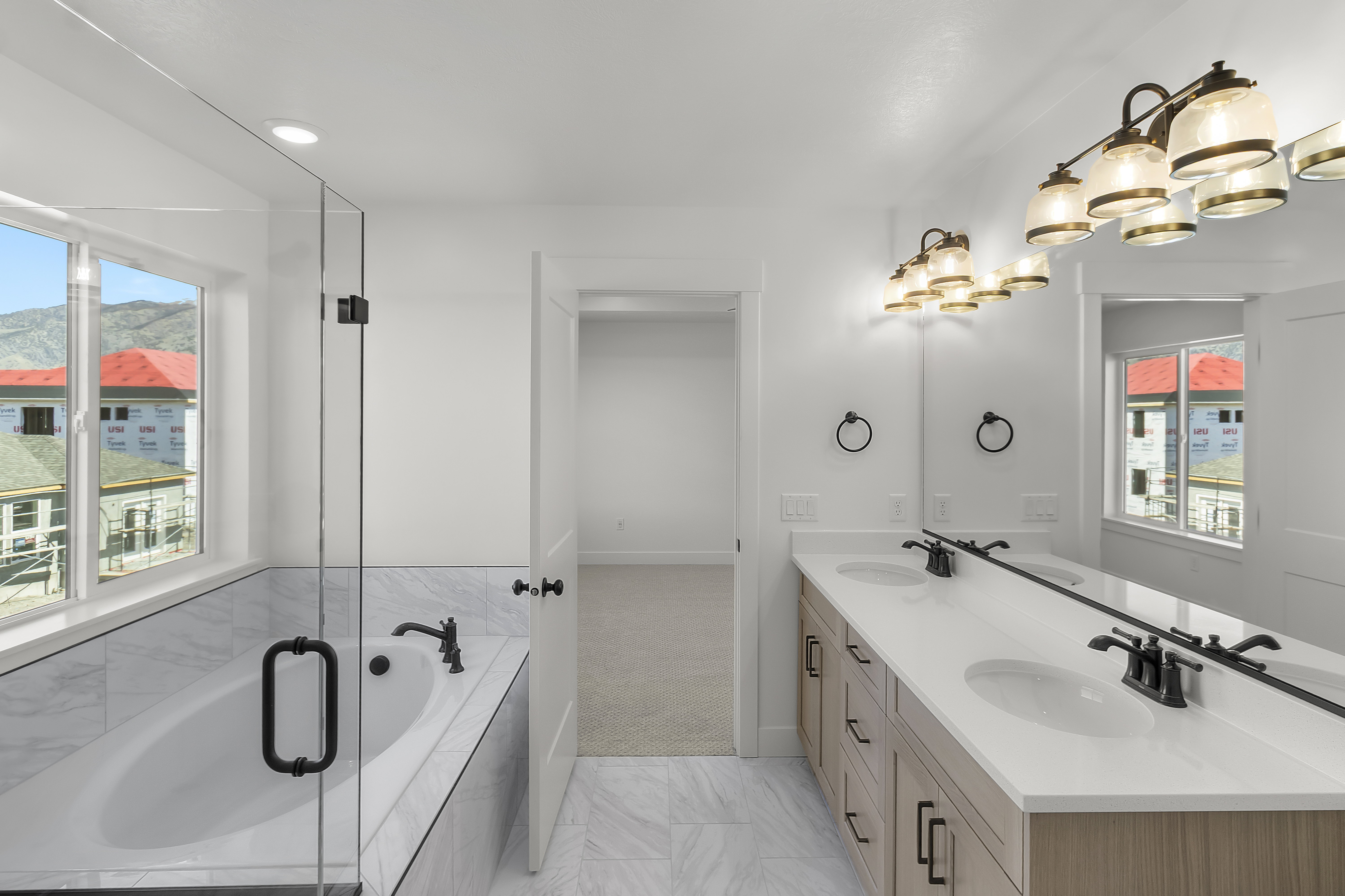 Bathroom featuring a built-in soaking tub with surrounding tile, a frameless glass shower enclosure, and a dual-sink vanity with light wood-finish cabinetry, white countertops, and matte black hardware