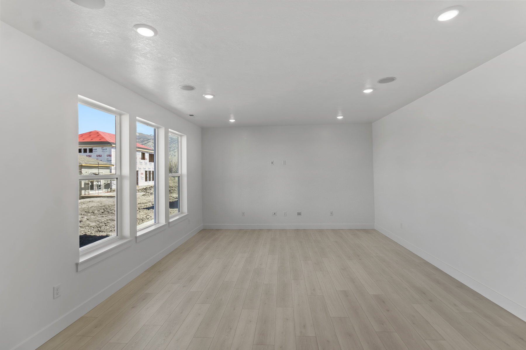 Spacious room featuring light wood-finish flooring, recessed lighting, and a series of three large windows providing abundant natural light